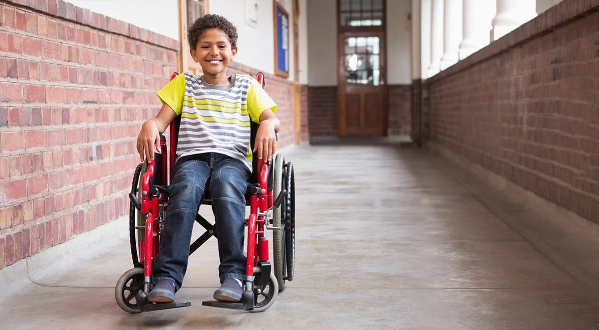 Child in wheelchair smiling in a school hallway
